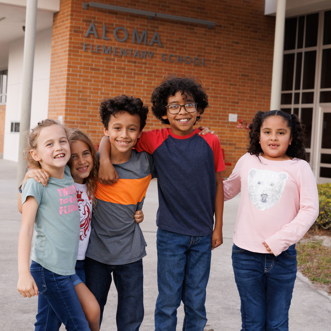 Group of diverse children posing in front of their elementary school.