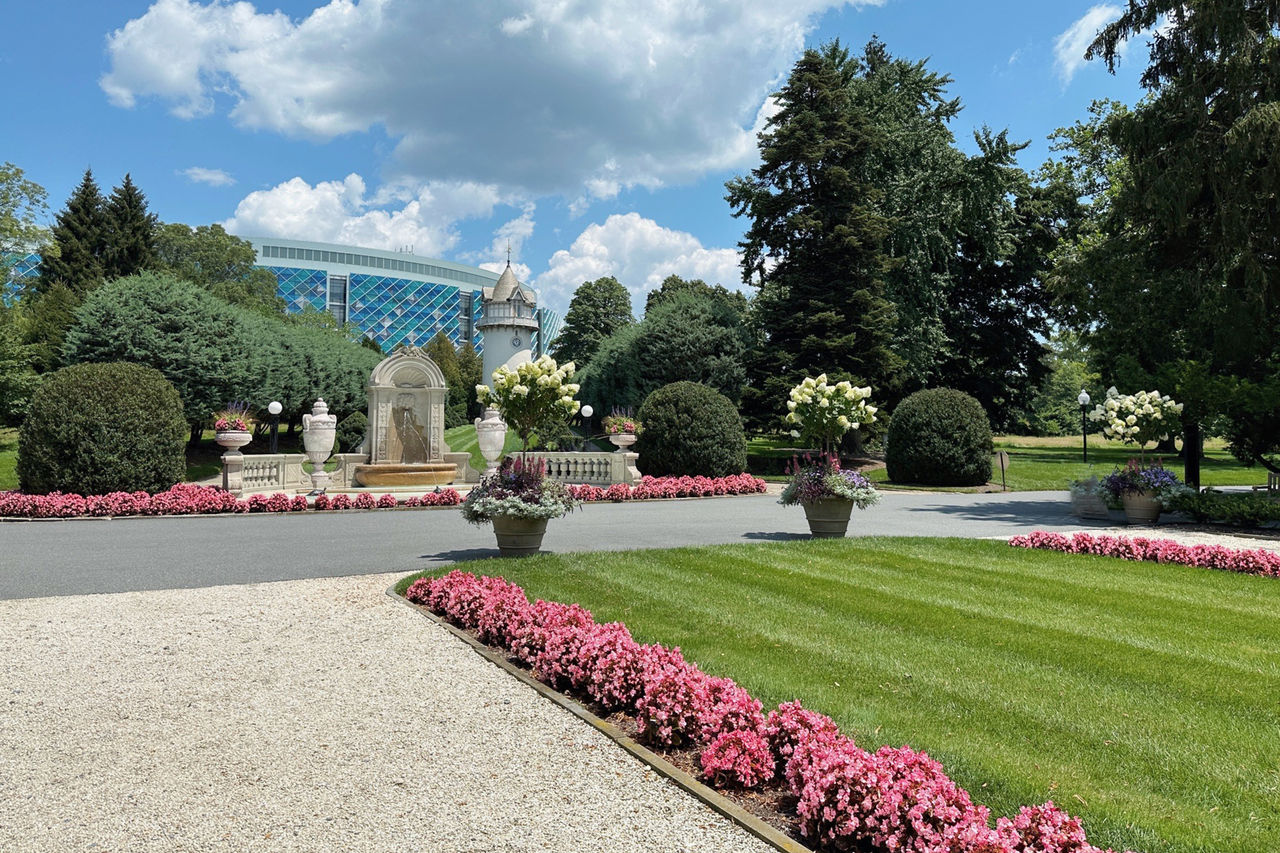 A point-of-view from the entrance of Nemours Estate shows that Nemours Children's Hospital, Delaware is on the other side of the gate, with beautiful gardens and trees in between. 