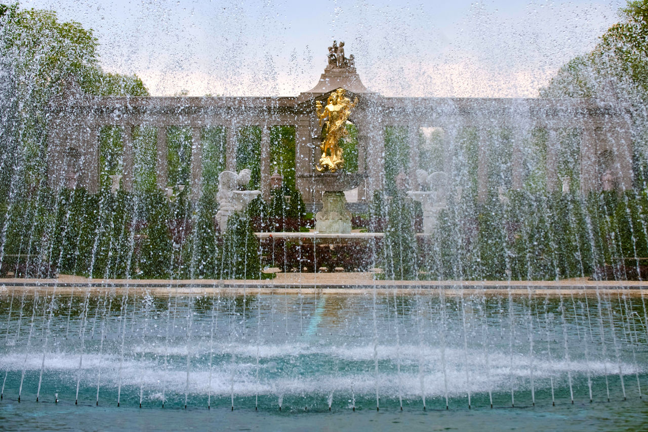 Sunset at the Reflecting Pool fountain with the gold Statue of Achievement in the center and the building in the background. 