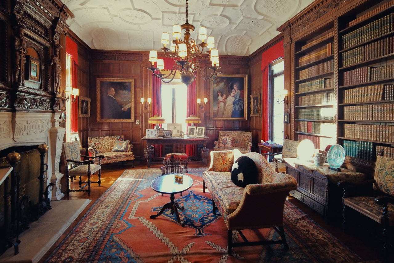 A library with orange walls and carpet, built-in bookshelves, a few pieces of furniture and a very large fireplace